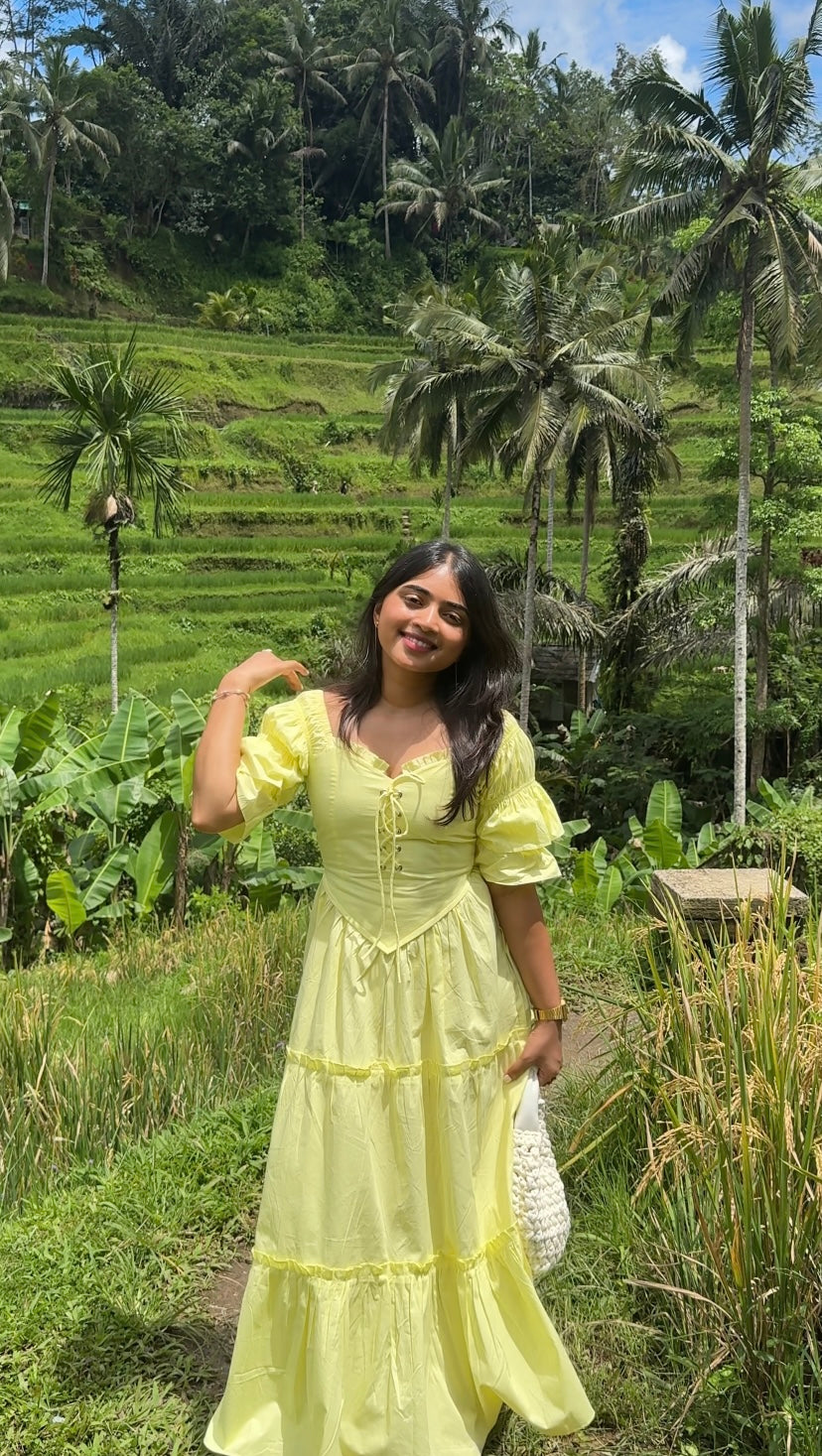 Woman in a yellow dress standing in a lush green field with rice terraces and palm trees.